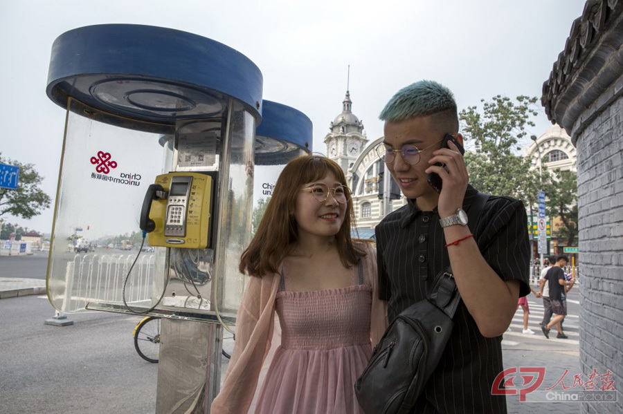 4-07,2018年摄于北京，前门。一对恋人边打手机边走过已经废弃的电话亭。李阜东(中国)摄.jpg